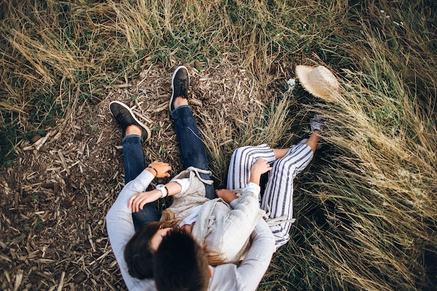 Прекрасная пара обниматься, целоваться и улыбаться на фоне неба, сидя на траве. Вид сверху