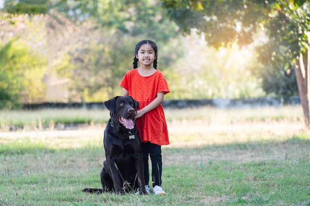 A lovely Southeast Asian child girl in red outfits plays with her big dog in the back or front yard in the evening. Pet lover concept