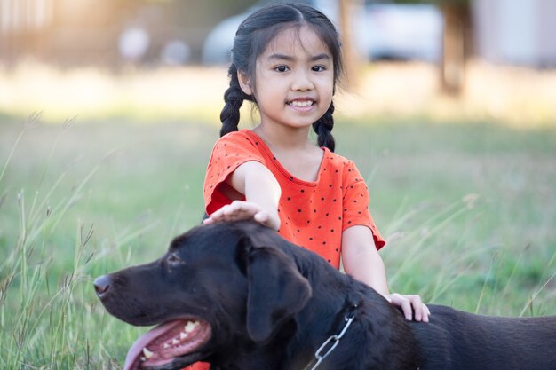 A lovely Southeast Asian child girl in red outfits plays with her big dog in the back or front yard in the evening. Pet lover concept