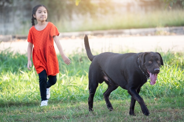 A lovely Southeast Asian child girl in red outfits plays with her big dog in the back or front yard in the evening. Pet lover concept