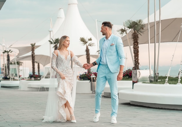 Lovely wedding couple groom and bride relax in the shore of the sea embracing holding hands