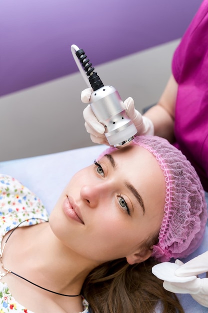 Lovely woman getting skin lifting treatment. Attractive girl receiving facial skin tightening procedure at beauty salon. Professional cosmetologist doing hardware skin treatment.