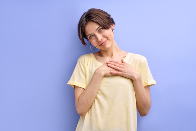 Lovely woman holding hands on chest feeling thanks gratitude cutely reacting at something in casual ...