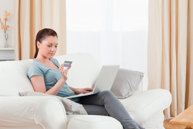 Lovely woman making an online payment with her credit card while sitting on a sofa