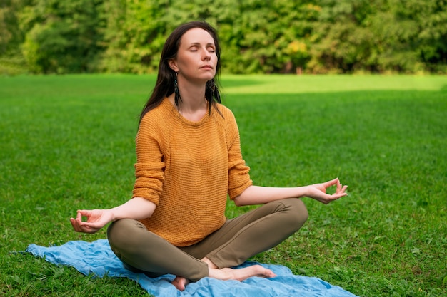 A lovely woman meditates sitting on the green grass in the Park