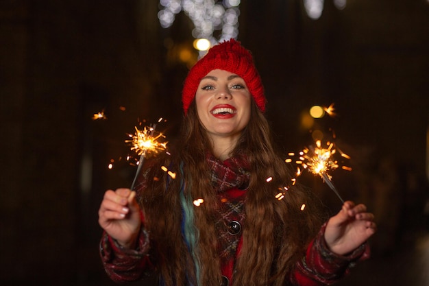 Lovely woman in red hat having fun with sparkling lights outdoor in the evening