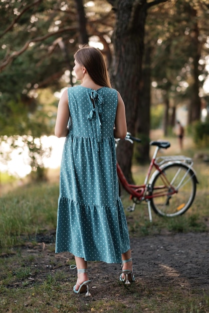 Lovely woman in summer dress on forest road with bicycle