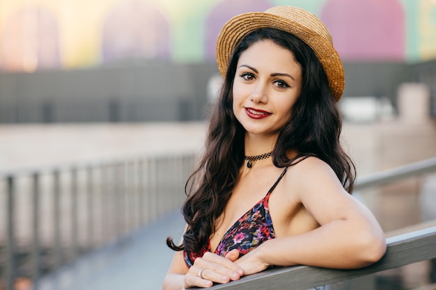 Bella donna con i capelli lunghi scuri, aspetto accattivante che indossa cappello e vestito estivo