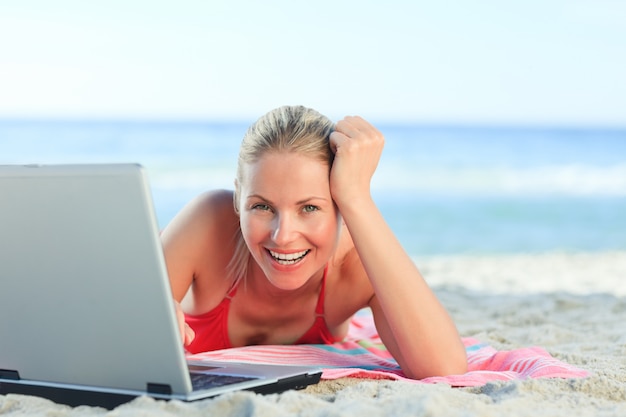 Bella donna che lavora sul suo computer portatile in spiaggia