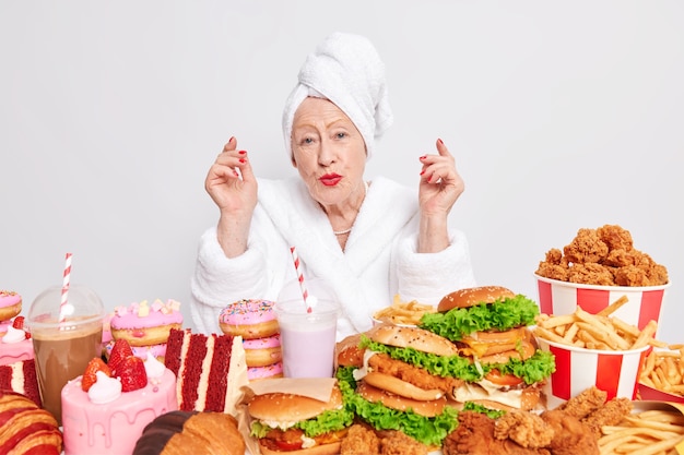 Lovely wrinkled lady enjoys cheat meal day surrounded by junk food