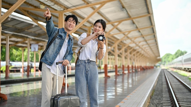 素敵なアジア人の若いカップルが駅で電車を待っています