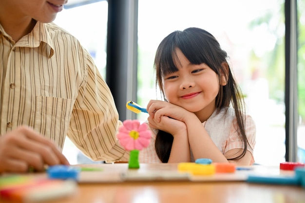 Lovely young Asian girl admiring a cute flowers play dough having fun time with her dad