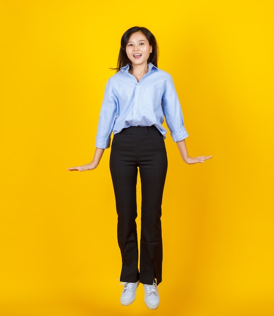 Photo lovely young asian girl jumping and freezed in the air with excited and cheerful face on yellow background.