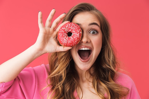 사랑스러운 젊은 금발의 여자, 도넛을 들고 분홍색 벽 위에 고립 된 서