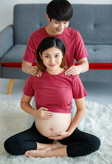 Lovely young couple. A pregnant woman smiling sitting on a floor resting after a workout. Young husband sitting behind his wife doing massage on her shoulder.