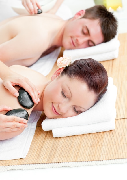 Photo lovely young couple receiving a back massage with hot stones