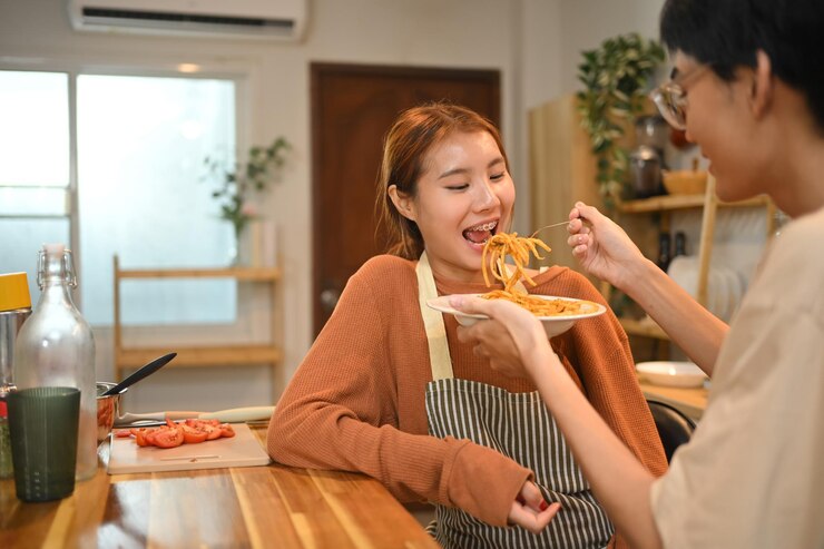 Photo キッチンで一緒に食事を楽しんでいるスパゲッティの皿を共有する可愛い若いカップル