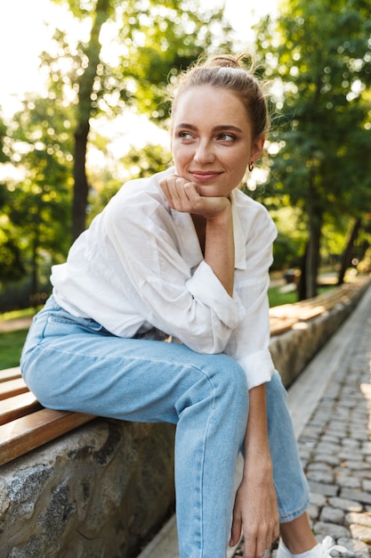 都市公園のベンチに座ってカジュアルな服を着た素敵な若い女の子