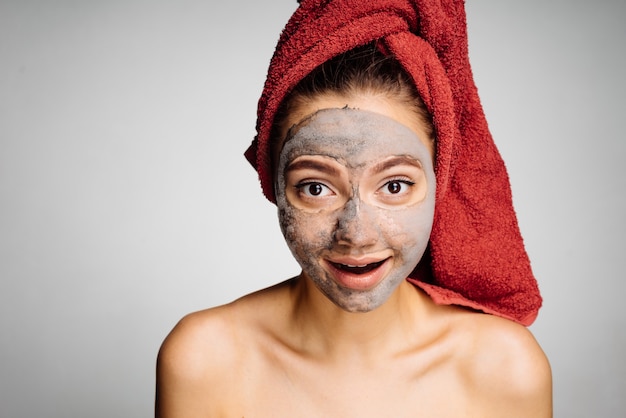 Lovely young girl with a red towel on her head has put a useful mask on her face, day spa