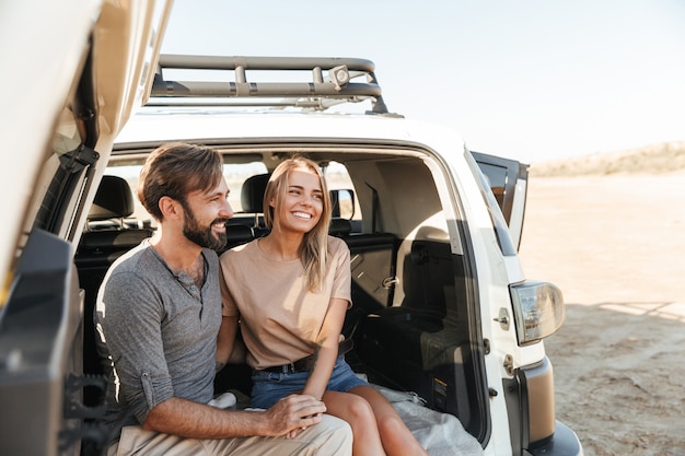 Photo lovely young happy couple sitting in the back of their car at the beach, embracing