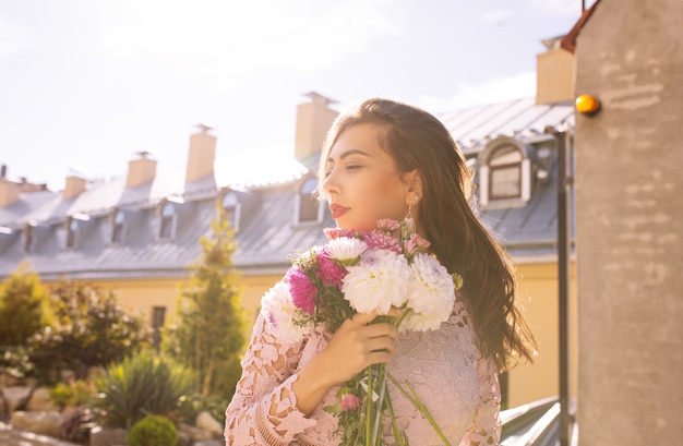 Lovely young model in pink dress with flowers in hands on a background of city