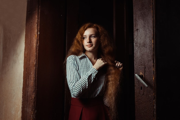 Lovely young red haired model with long lush hair. Woman posing in a dark room