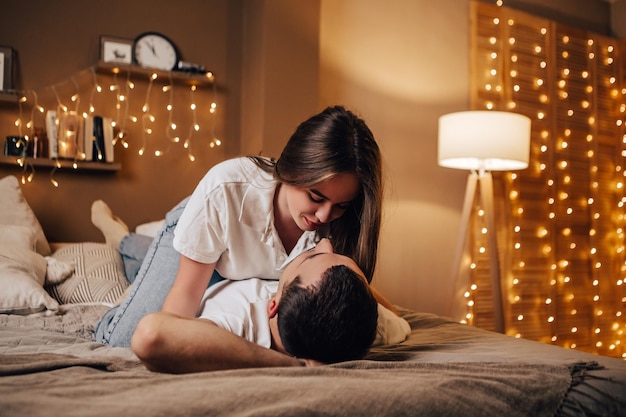 Lovely young romantic couple lying on bed garlands kissing hugging home cosy interior atmosphere