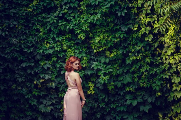 Bella giovane donna in un vestito rosa e capelli rossi, in attesa di un appuntamento