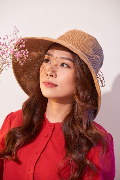 A lovely young woman in summer dress and straw hat posing while holding bouquet flowers