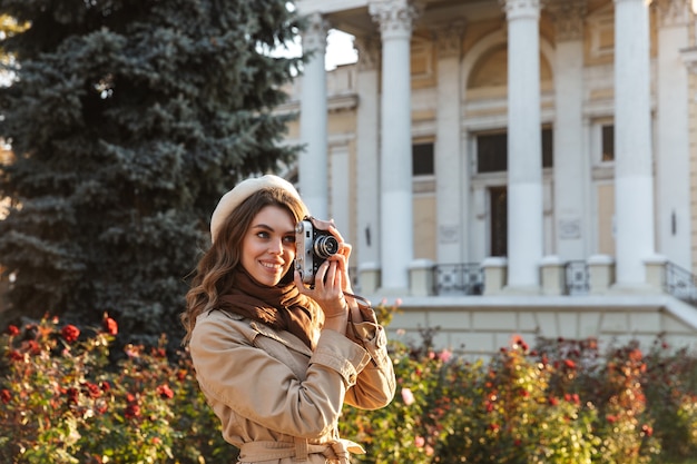 사진 카메라를 사용하여 야외에서 산책하는 코트를 입고 사랑스러운 젊은 여자