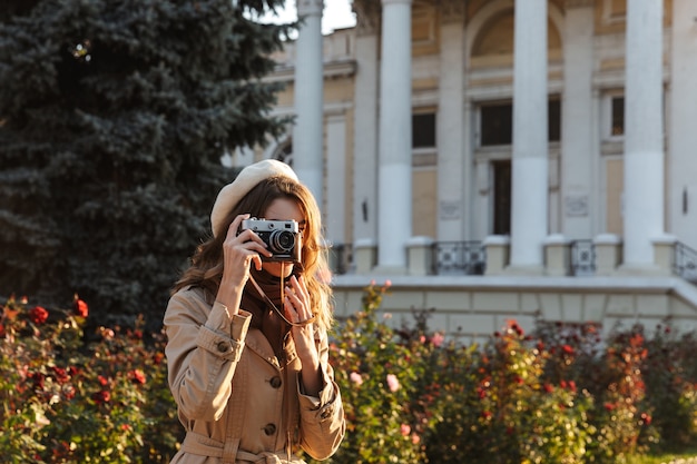 사진 카메라를 사용하여 야외에서 산책하는 코트를 입고 사랑스러운 젊은 여자