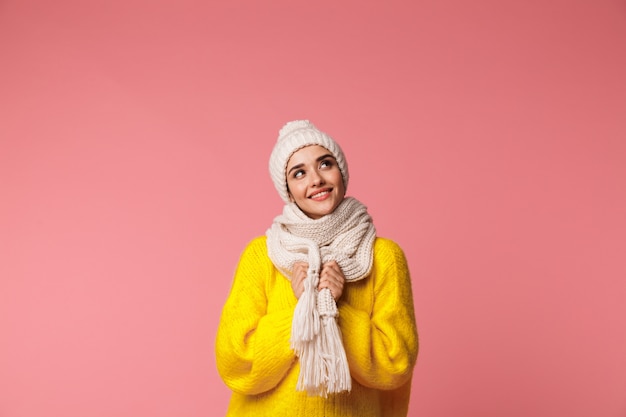 Bella giovane donna che indossa cappello caldo e sciarpa in piedi isolato su rosa, in posa