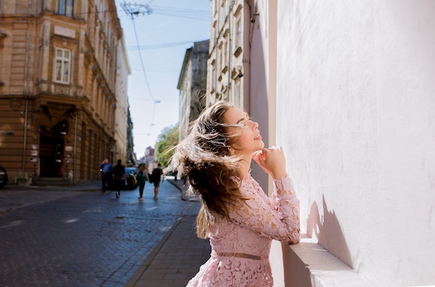 Lovely young woman with beautiful hair in wind posing at the street in sunny day. Woman wearing fashionable lace dress