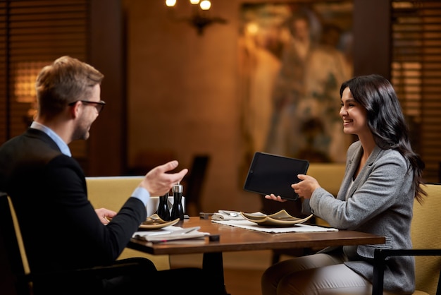 Lovely young woman with tablet in hand talking to man