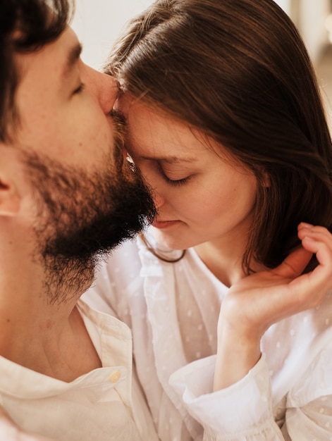 Foto ragazzo amante bacia la sua ragazza sulla fronte. abbracciare dolcemente il bacio. vestito in pigiama