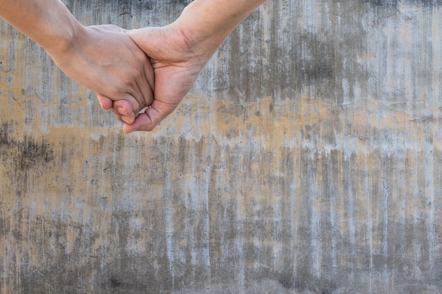 Lover hold hand on aged vintage gray cement wall texture background