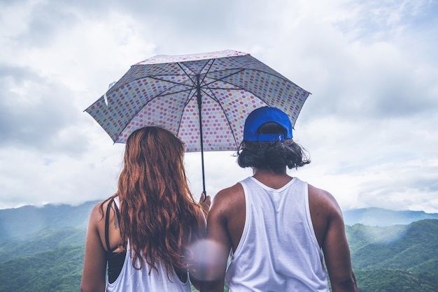 恋人の女性と男性のアジア人旅行。山の雨傘に立った