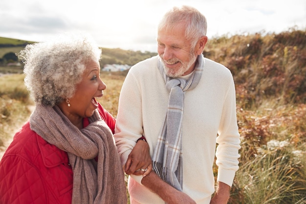 Photo loving active senior couple walking arm in arm through sand dunes on winter beach vacation