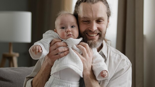 Loving adult bearded father holding baby newborn caring dad playing with little daughter son child