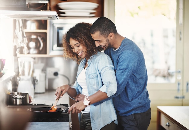 Loving and affectionate couple cooking breakfast lunch or dinner together in the kitchen while hugging Young Black American lovers preparing a meal at home on a fun weekend enjoying quality time