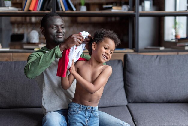 Loving africanamerican father dressing up his son on sofa