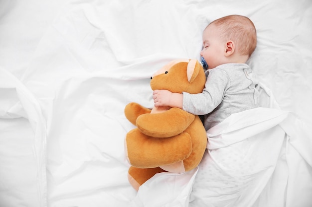 Photo loving baby with teddy bear sleeping on soft bed close up