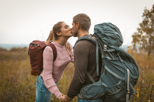 Loving backpackers kiss in the field outdoors. Happy couple of travelers