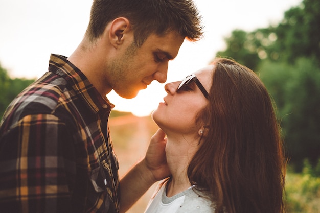 loving boyfriend kisses his girlfriend, looking into his eyes, sunset, outdoor, sun rays