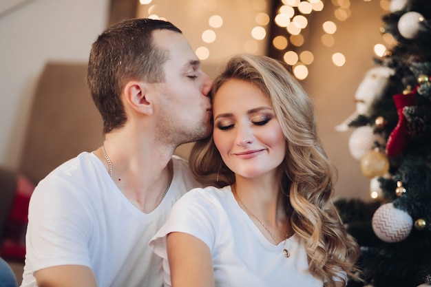 Loving boyfriend kissing girlfriend near Christmas tree 