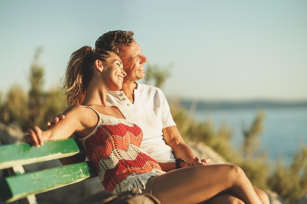 A loving couple are sitting on bench and enjoying a summer vacation near the sea beach.