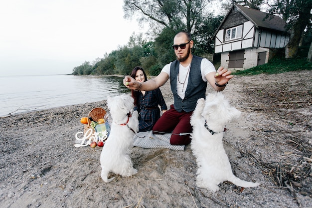 Photo loving couple on the beach playing with their white dogs