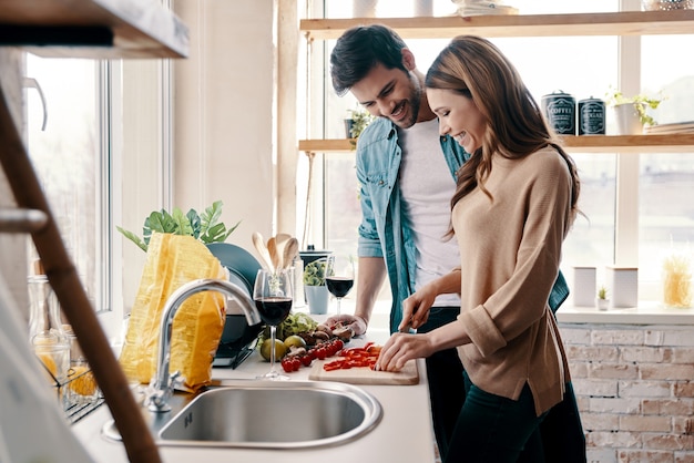 愛するカップル。自宅のキッチンに立って夕食を調理する美しい若いカップル