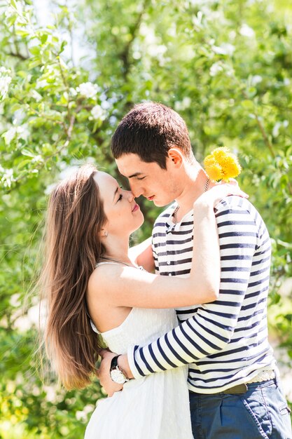 Loving couple under blossoming branches spring day. young adult brunette man and woman kissing in fresh blossom apple or cherry trees garden. sweet kiss