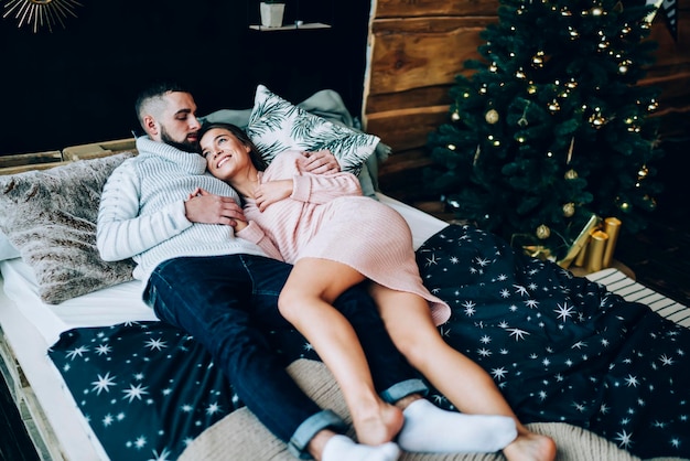 Loving couple embracing lying on bed with Christmas tree on background